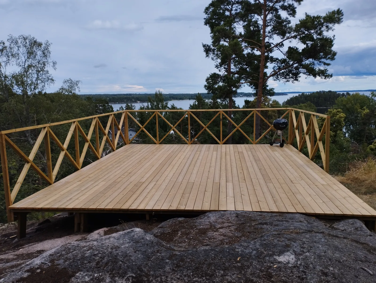 Träaltan med kryssräcke och utsikt över vattnet mellan tallarna.
