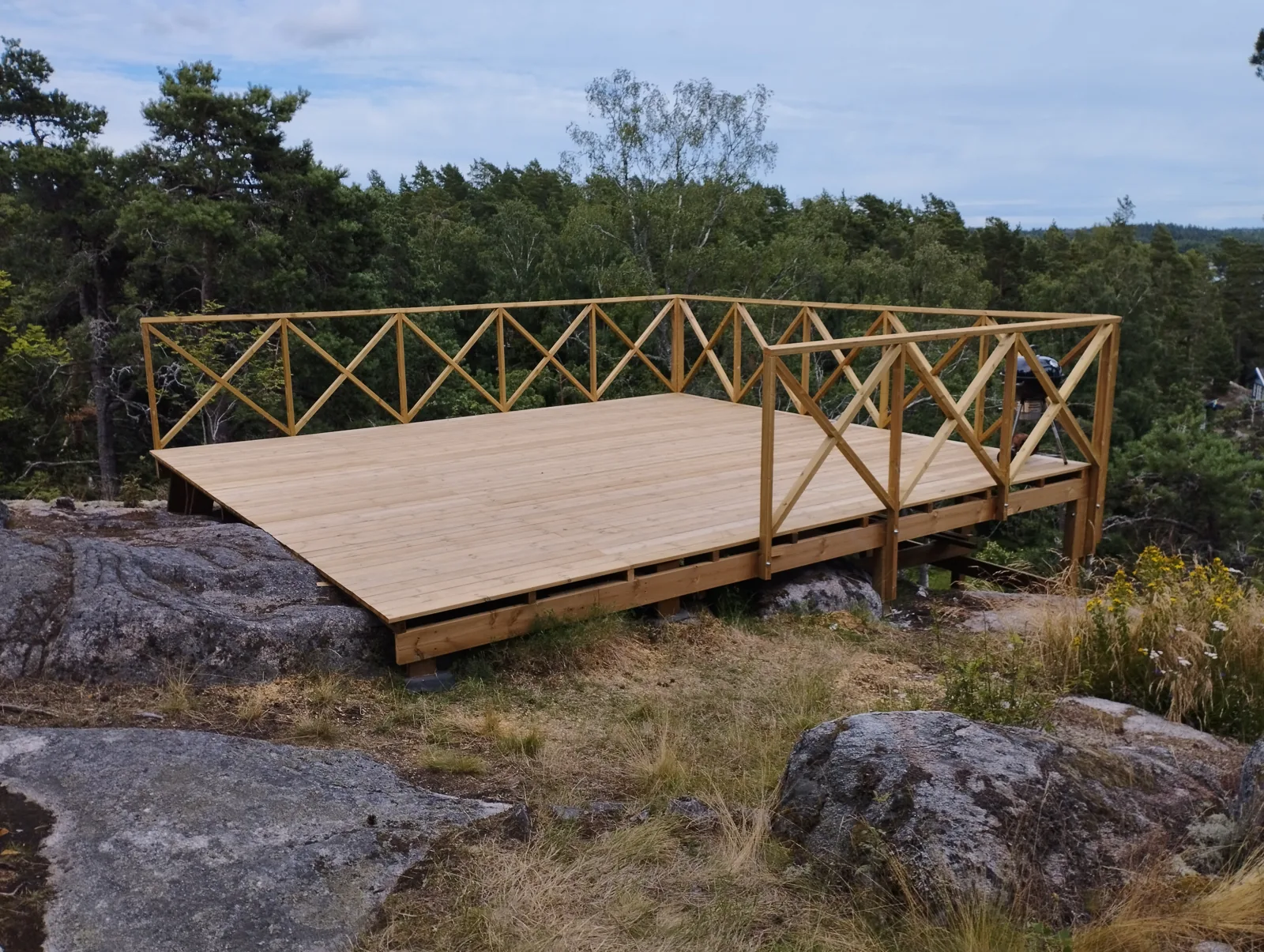 Färdig altan med räcke och trappa på en kuperad naturtomt.