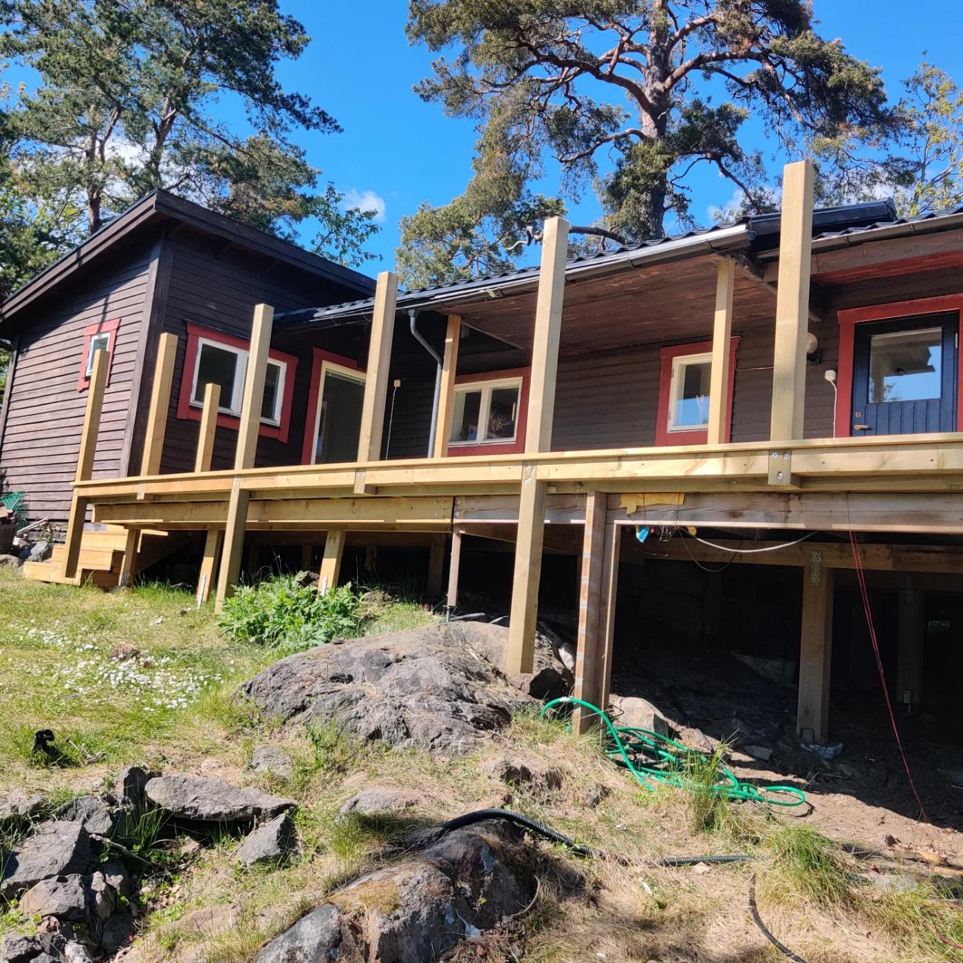 Synliga bärande trädelar och stolpar framför en träfasad ovanför ojämnt berg.